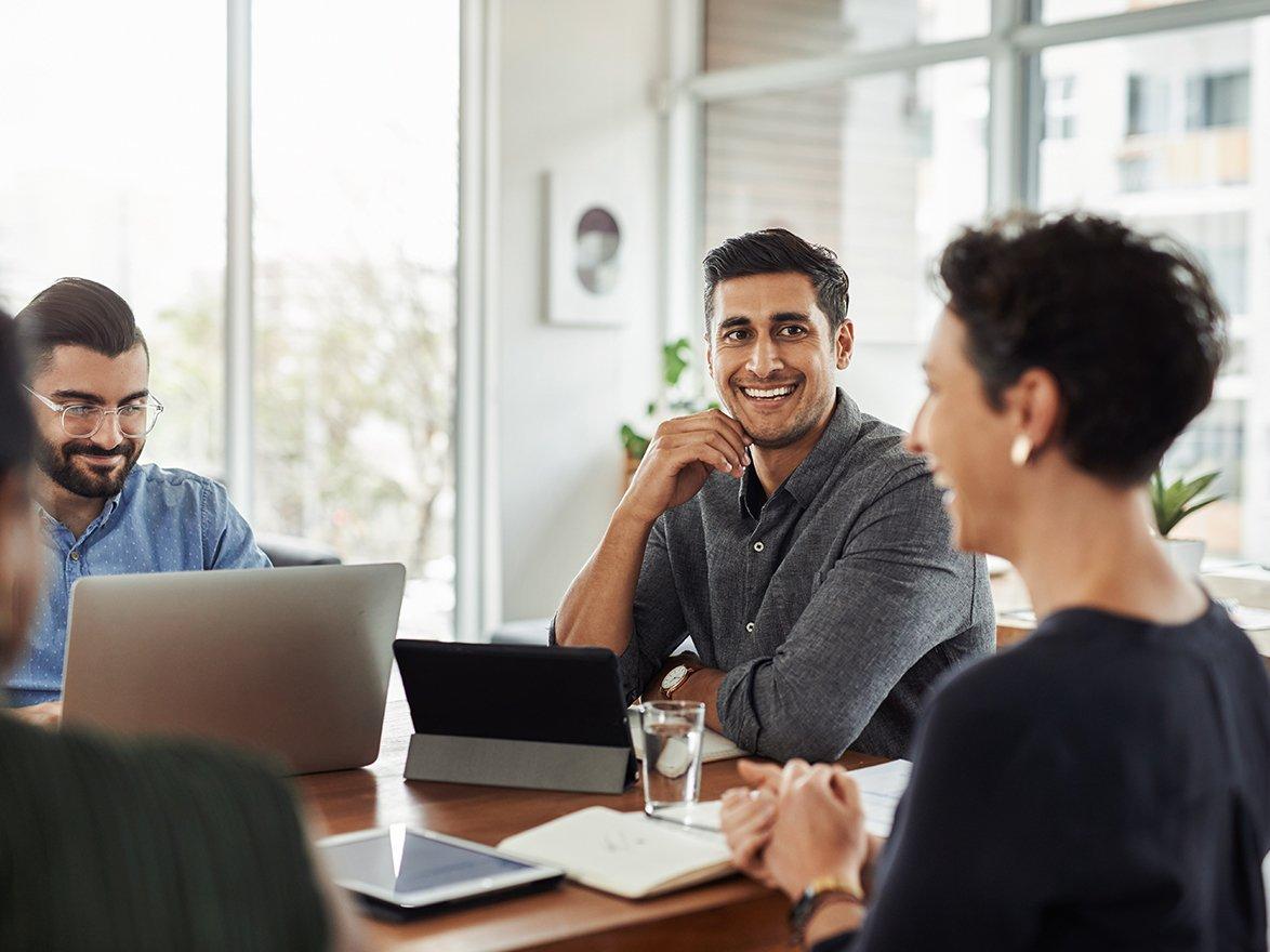 Four coworkers smiling and working together at a table with laptops