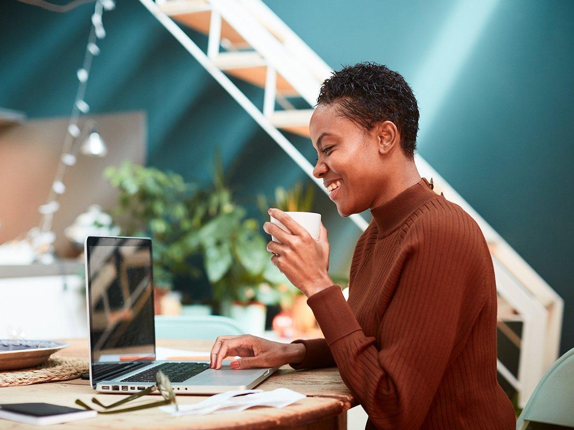 Coworker smiling while looking at her computer and drinking coffee